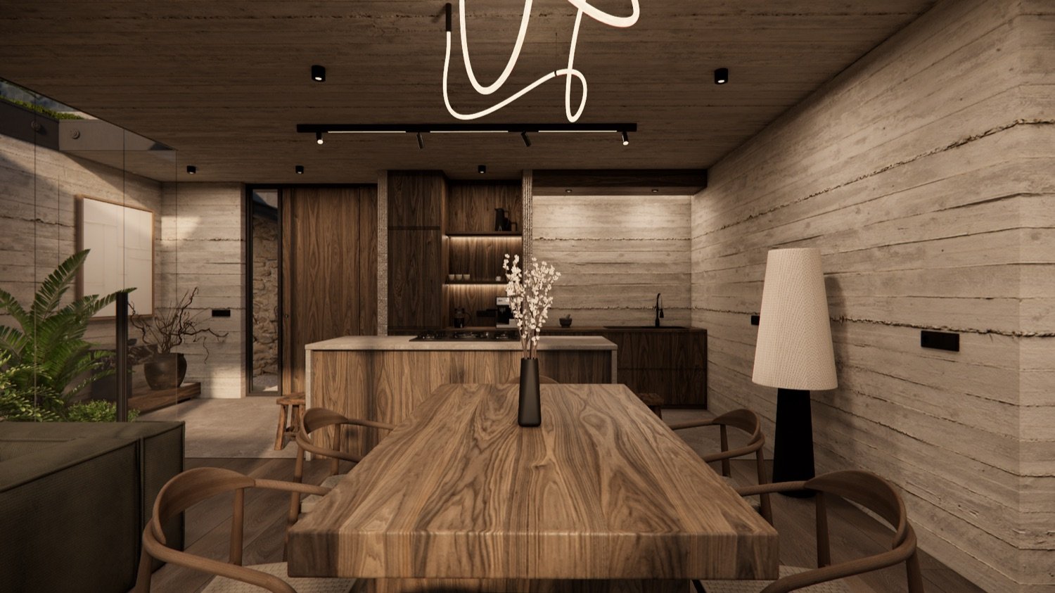 Dining room with a long solid-wood table, sculptural pendant light and the kitchen beyond in warm evening light.